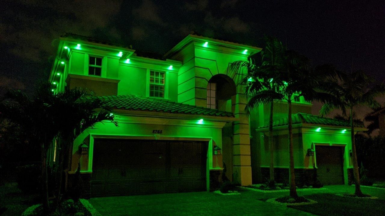 House exterior at night, lit with bright green lights along roof and doorway.