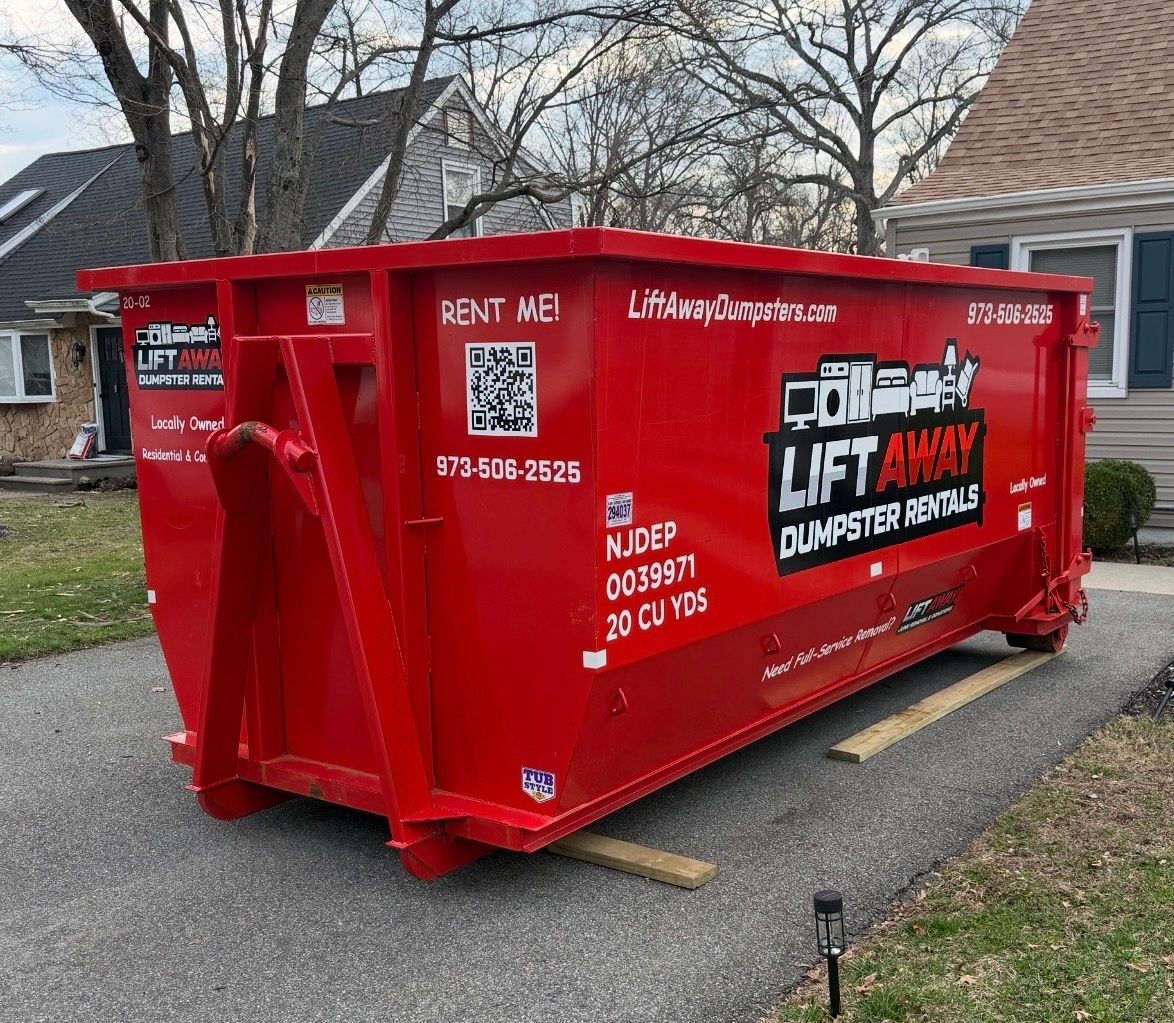 A bright red Lift Away dumpster rental unit sits on a residential driveway in front of a house.