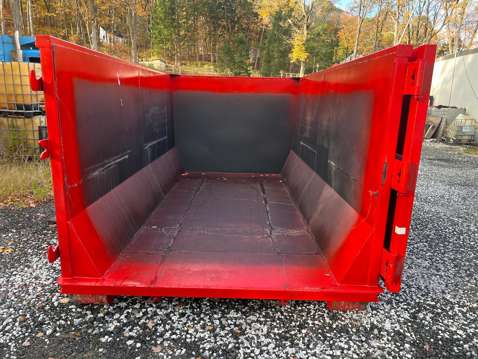 Red industrial waste container outdoors on gravel.