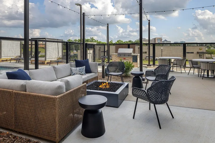 Outdoor rooftop patio with wicker seating, fire pit, and city skyline view under string lights