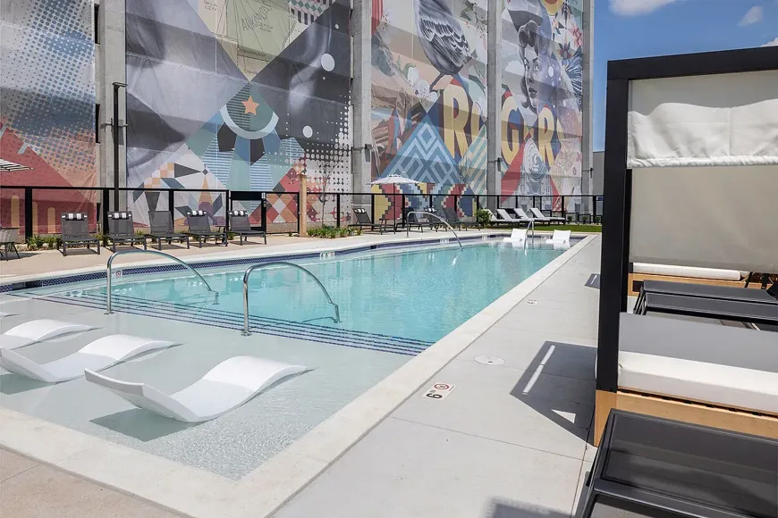 Outdoor rooftop pool with white lounge chairs beside a mural-covered wall.