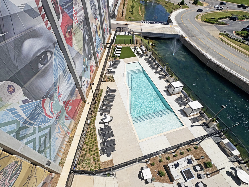 Rooftop pool and lounge area beside a canal, with a mural-covered building and highway nearby