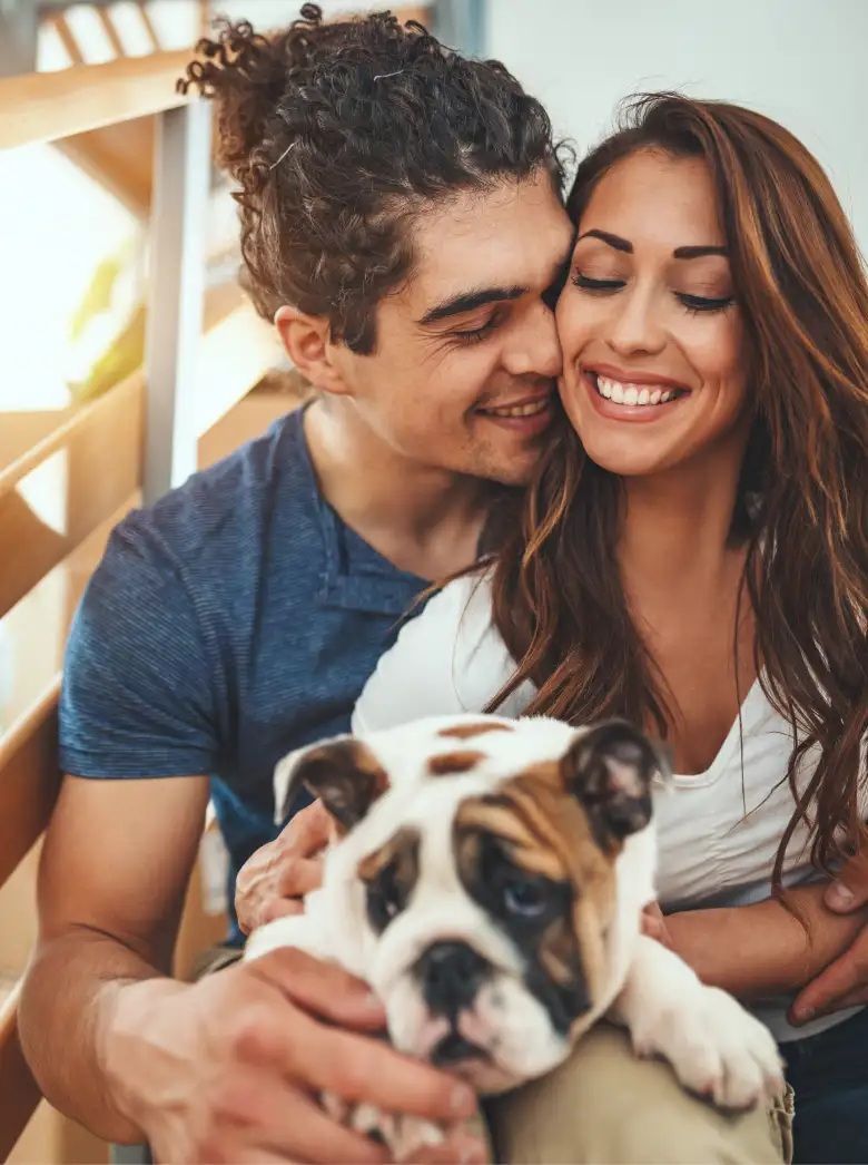 Smiling couple cuddling with a bulldog on a couch indoors
