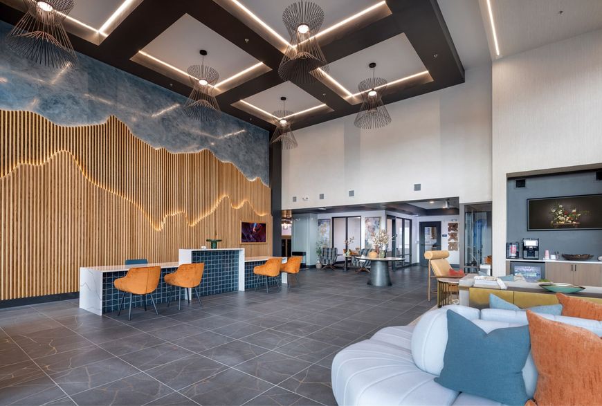 Modern hotel lobby with high ceilings, wood accent wall, blue chairs, and a white sectional sofa