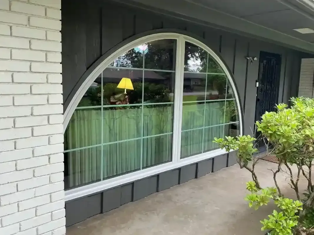 A large arched window with a white frame and grid pattern set in a dark gray paneled wall next to a white brick wall.