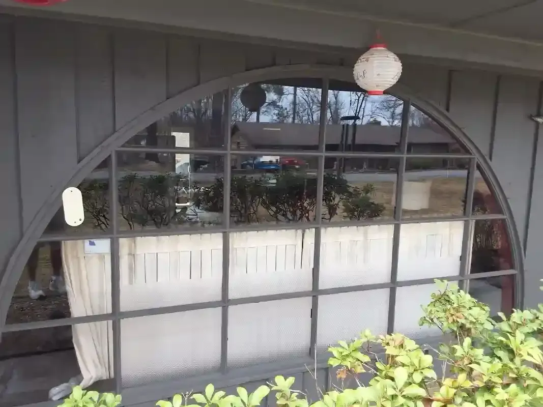 Arched window with a grid frame and a white curtain behind it, viewed from an exterior porch with hanging lanterns.