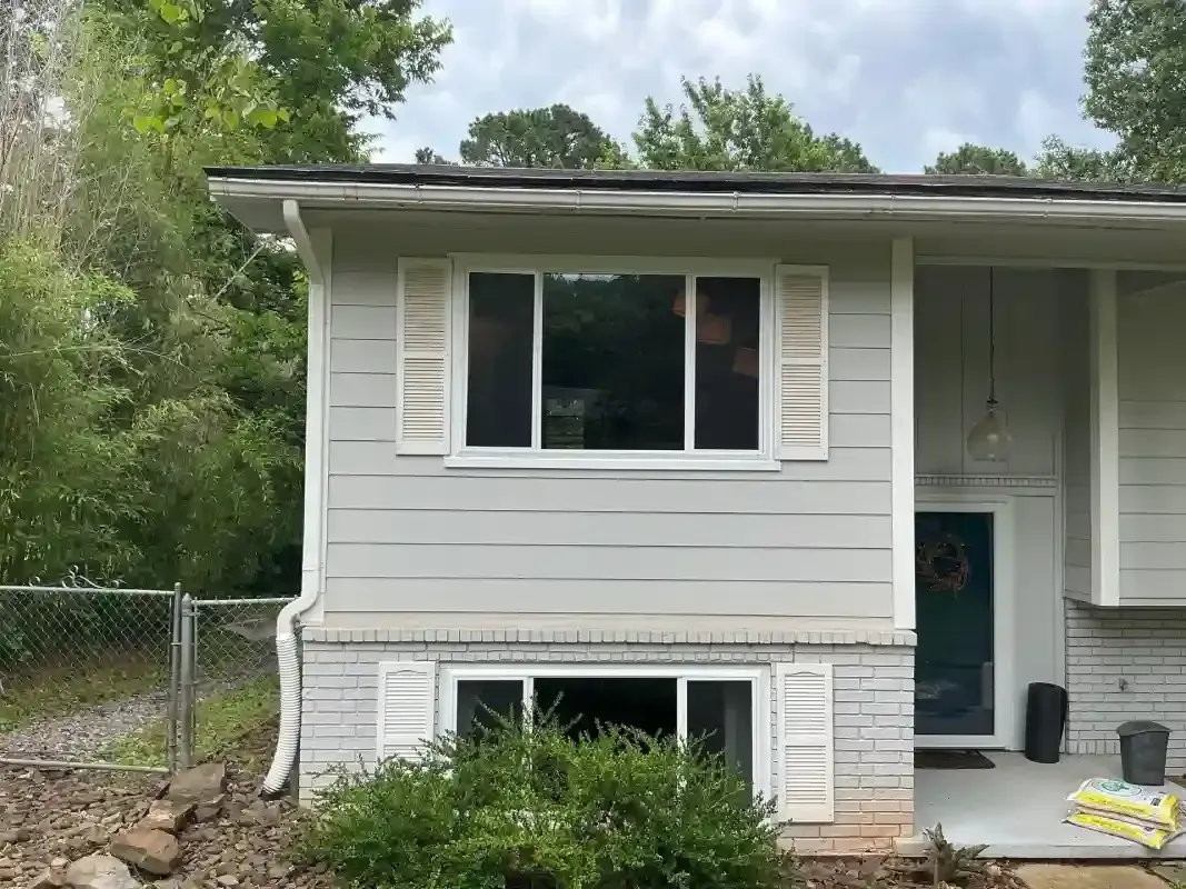 A single-story, gray house with white shutters on two windows, a brick lower section, and a covered front entryway.
