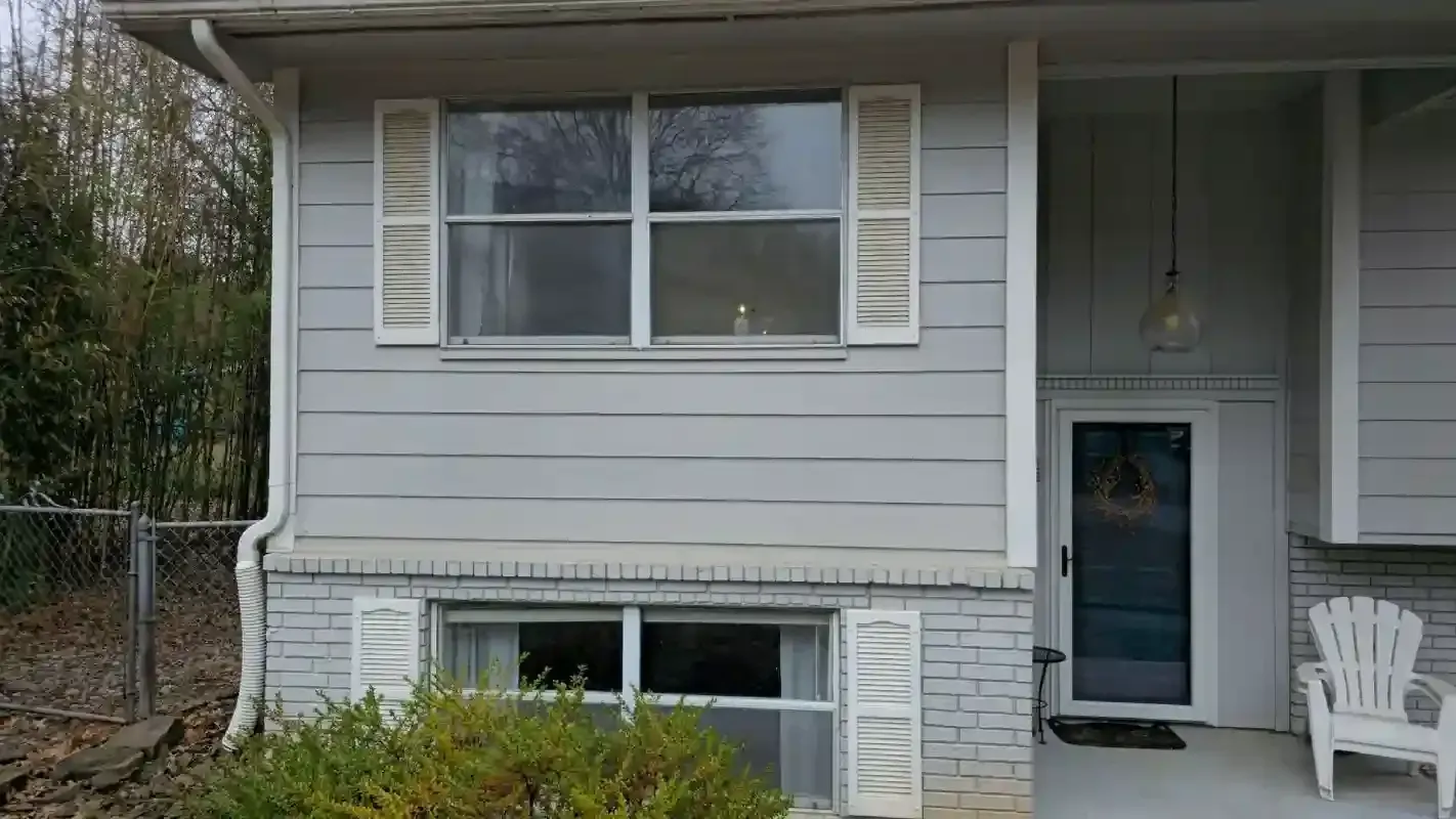 Light gray house exterior featuring a two-story window arrangement, white shutters, and a front entrance with a porch chair.