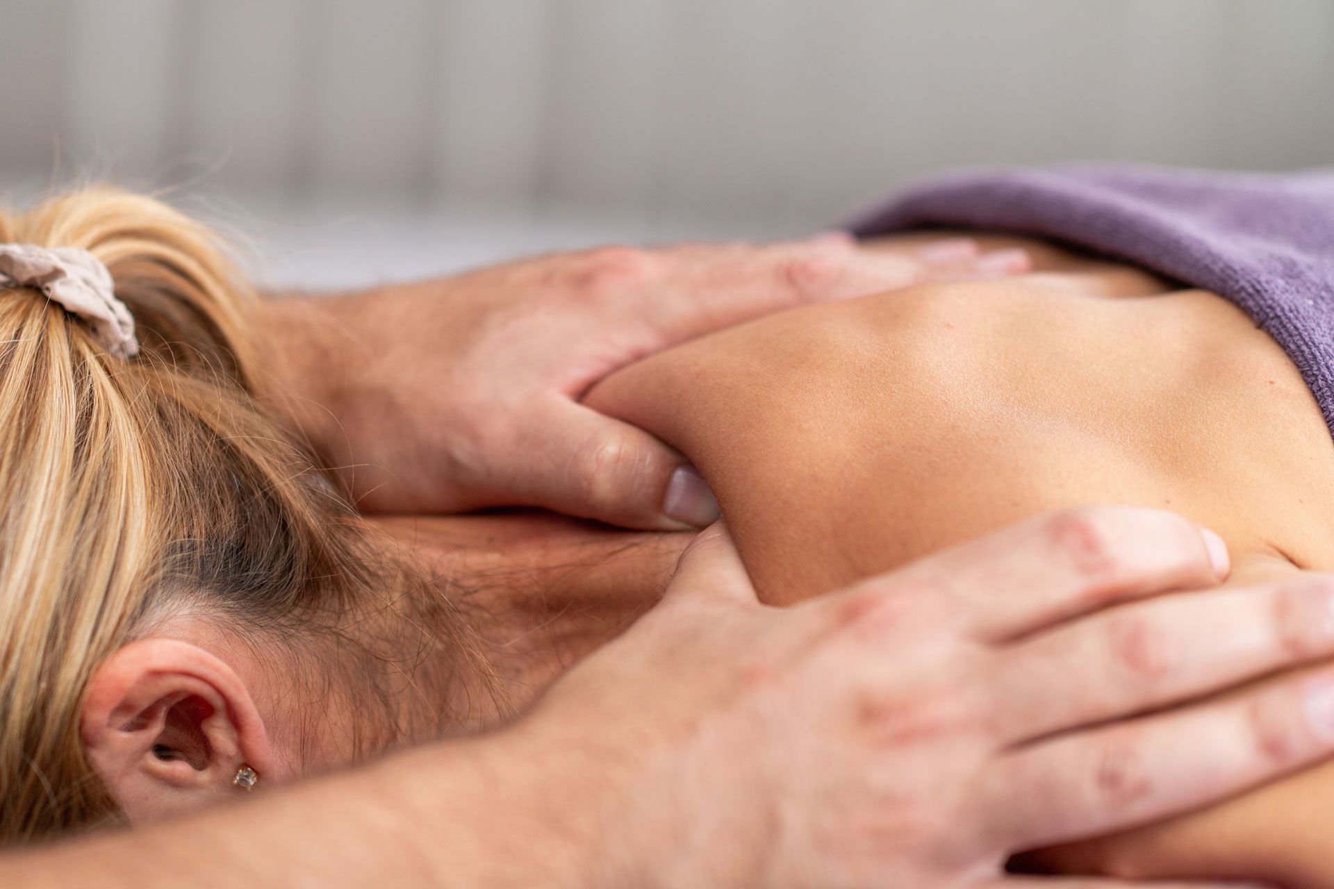 A massage therapist's hands kneading the shoulder and neck area of a person lying on a massage table.