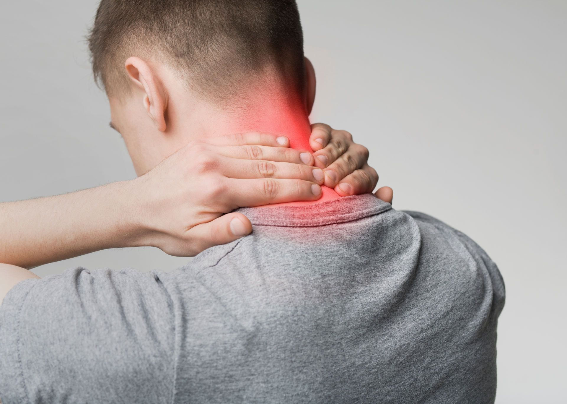 A person in a gray shirt holding their neck, which is highlighted in red to indicate pain.