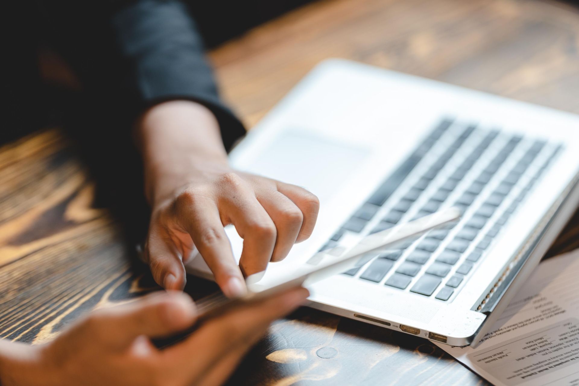 Hands using a tablet and laptop on a wooden table.