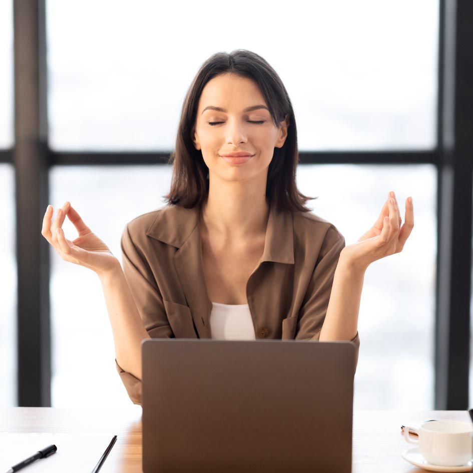 Yoga-Kurs im Gange; Frauen in Fitnesskleidung sitzen mit geschlossenen Augen und Händen in Gebetshaltung. Inneneinrichtung aus hellem Holz.