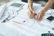 Hands drafting architectural plans on a desk with blueprints, ruler, calculator, and tablet Hands drafting architectural plans on a desk with blueprints, ruler, calculator, and tablet