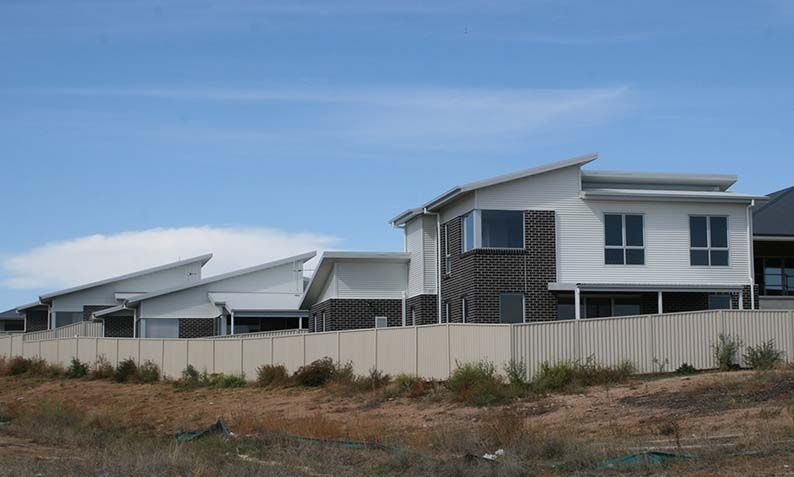 Modern white house under construction behind a fence in a grassy suburban area