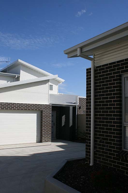 Modern suburban driveway beside white garages and dark brick house under a blue sky Modern suburban driveway beside white garages and dark brick house under a blue sky