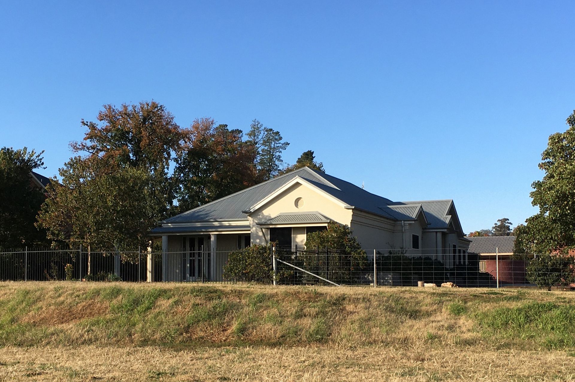 Small beige house with a gray roof behind a grassy embankment under a clear blue sky.