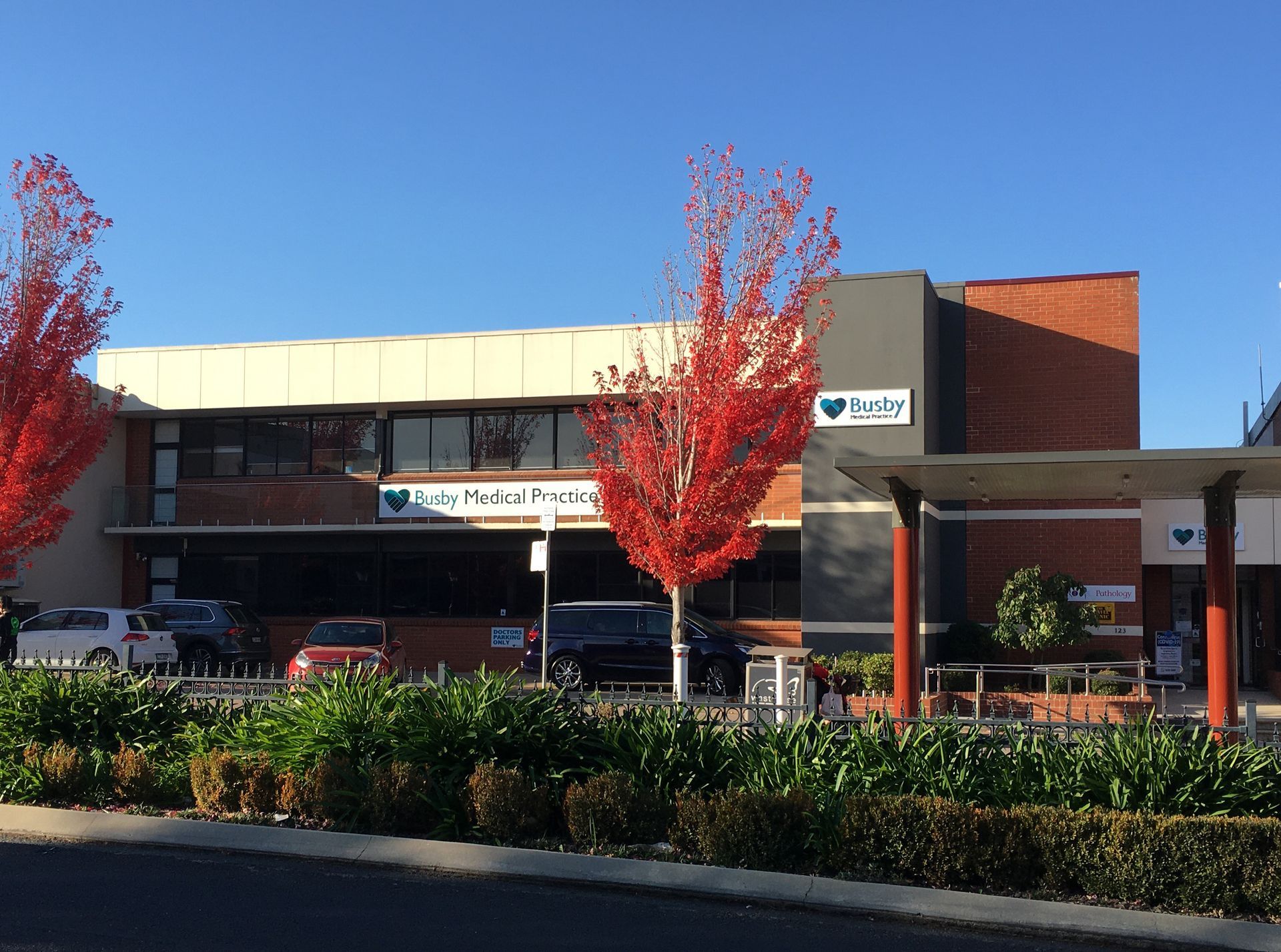 Street view of a brick building with autumn trees and a covered entrance under a clear blue sky