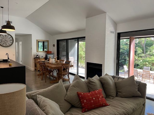 Bright open-plan living and dining room with gray sofa, dining table, fireplace, and sliding glass doors to a garden.