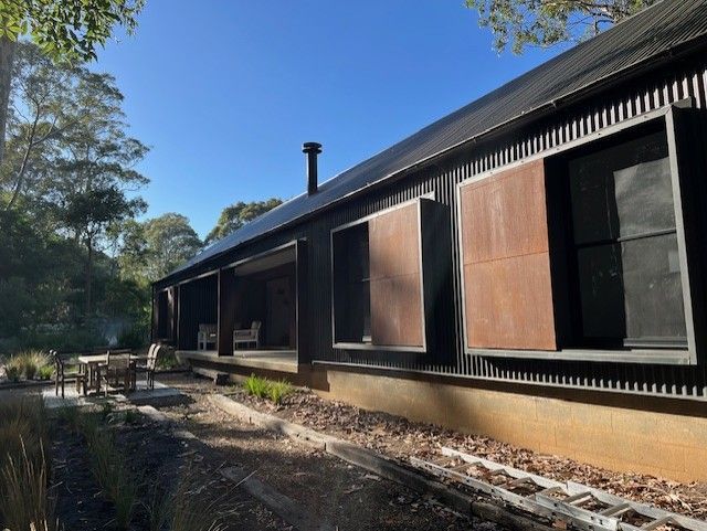 Long, sunlit wooden building with closed shutters beside a stone-lined path and trees Long, sunlit wooden building with closed shutters beside a stone-lined path and trees