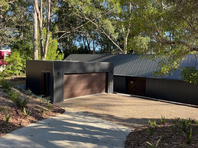 Modern house with dark roof and garage, set among trees with a curved driveway and path
