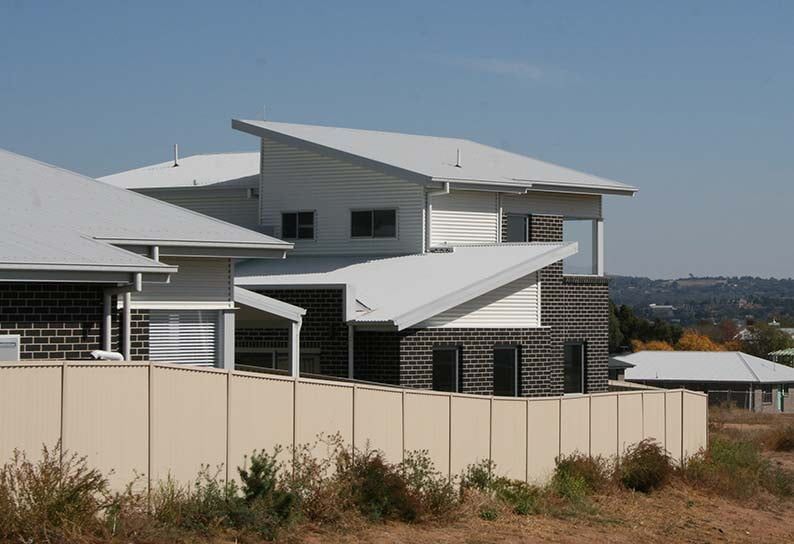 Modern white house with sloped roofs behind a beige fence in a dry suburban setting Modern white house with sloped roofs behind a beige fence in a dry suburban setting