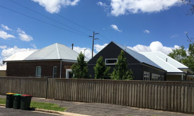 Suburban houses with gray roofs behind a tall wooden fence under a bright blue sky. Suburban houses with gray roofs behind a tall wooden fence under a bright blue sky.