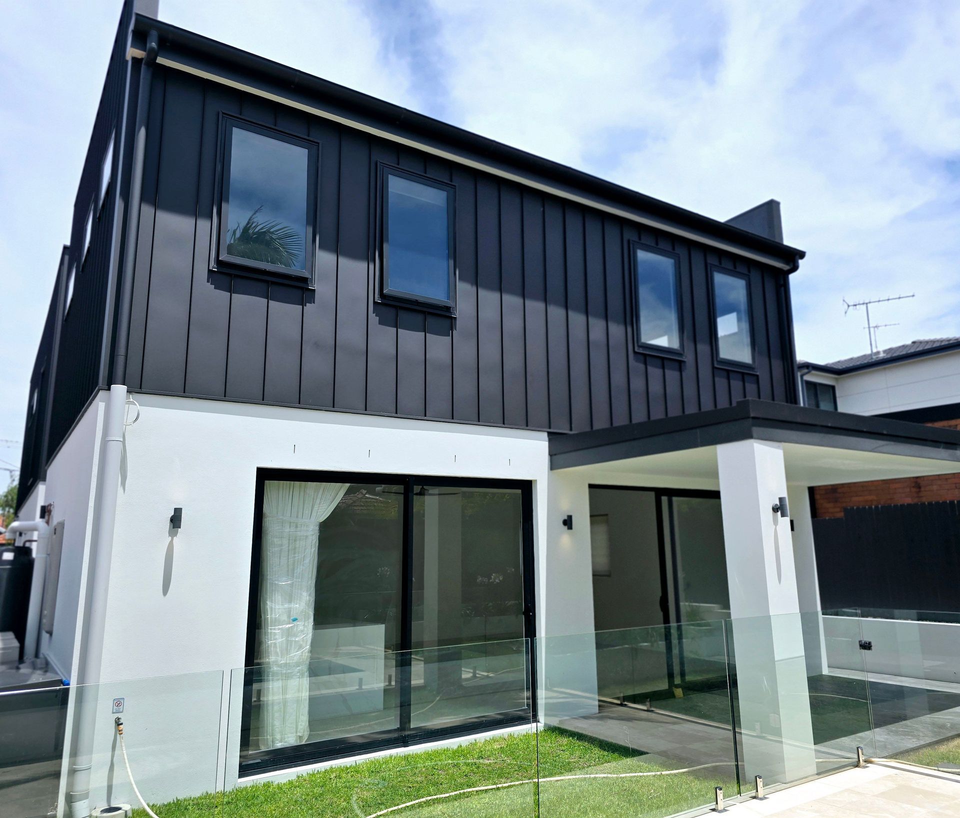 Modern two-story house with black upper siding, white lower walls, and large glass sliding doors.