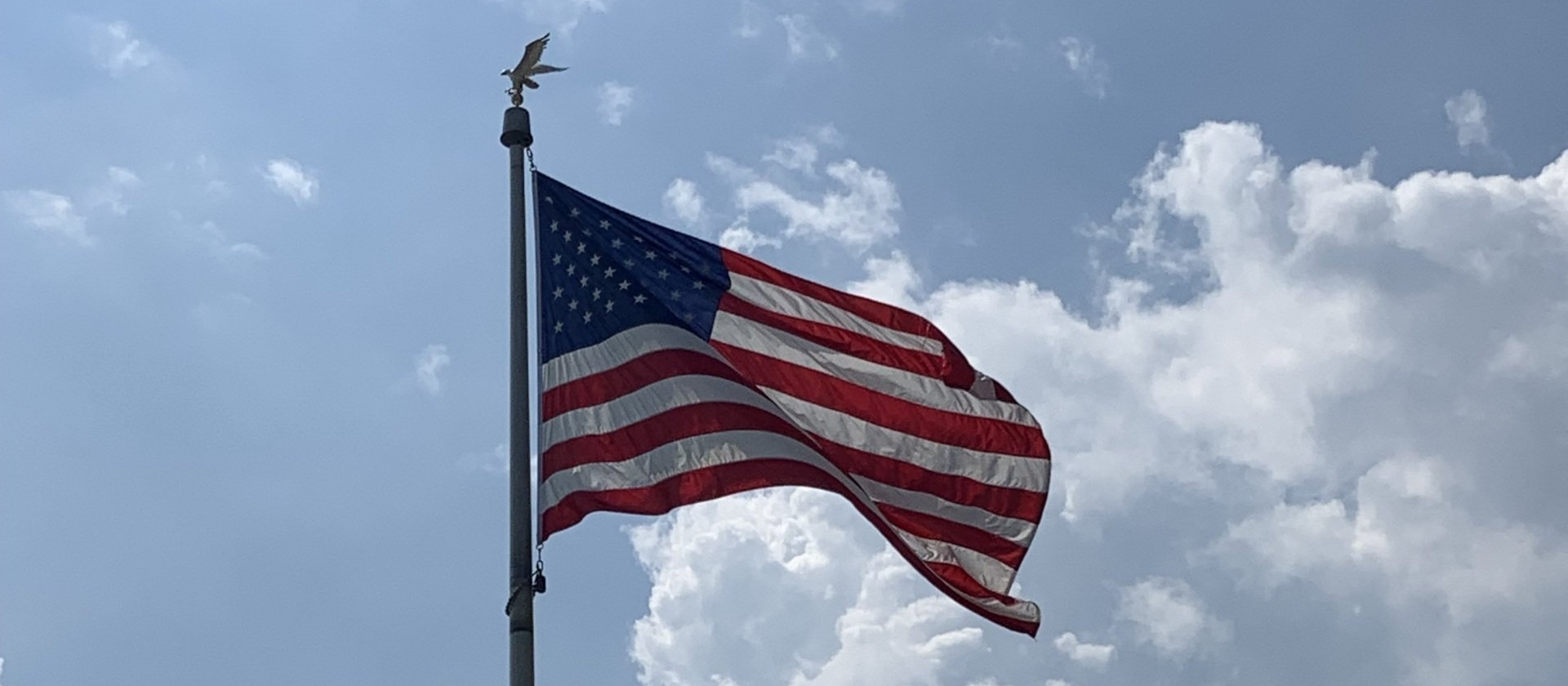 An american flag is waving in the wind against a cloudy blue sky.
