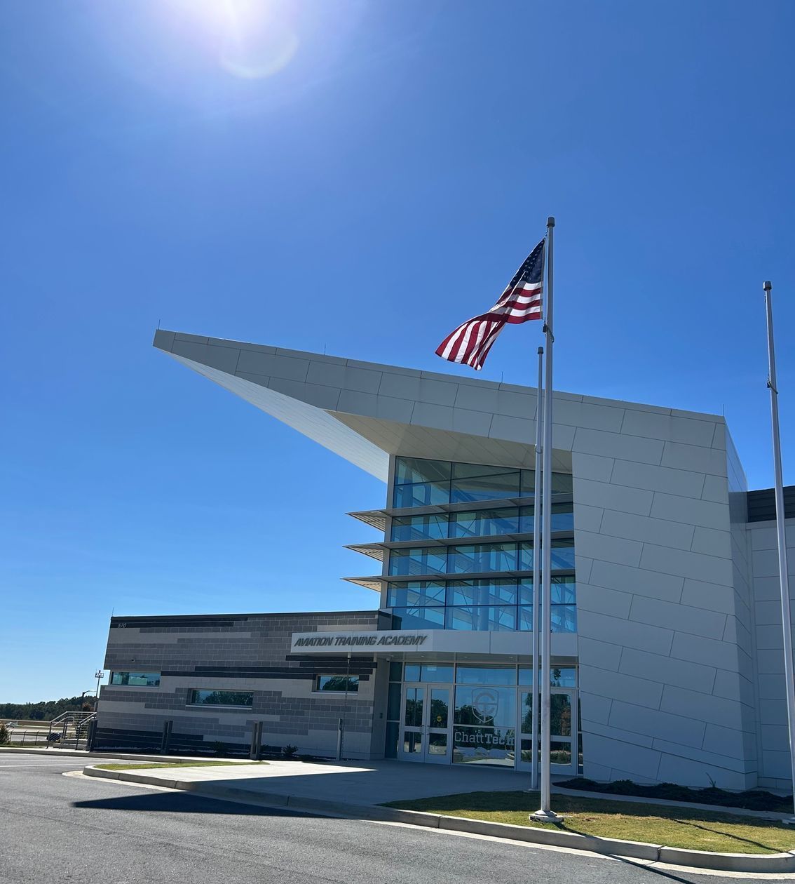 A large flagpole outside of a large, slanted, white building