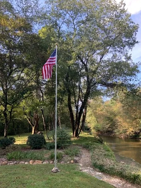An american flag is flying on a pole in front of a river.