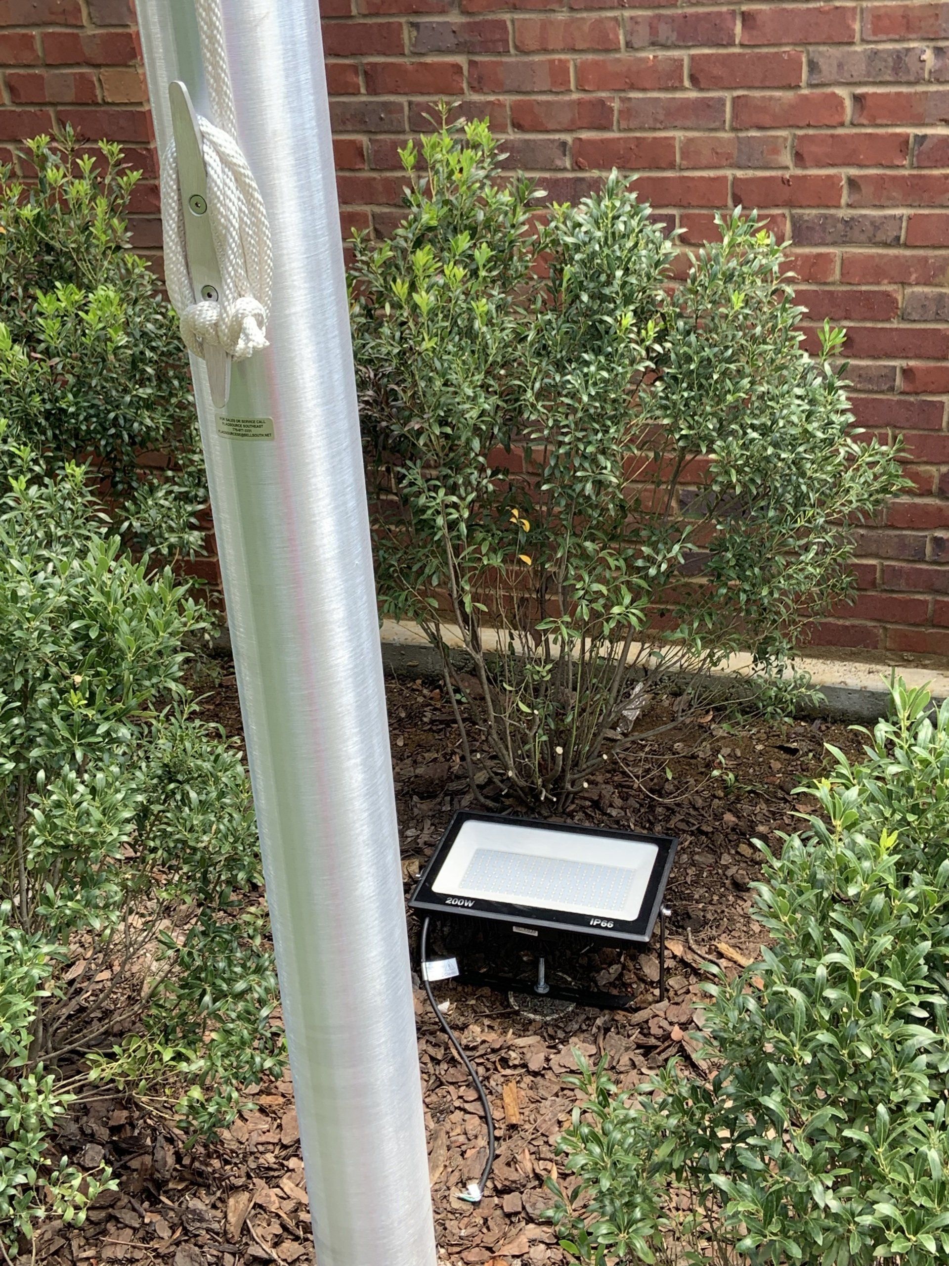 A light is sitting in the dirt next to a flag pole.