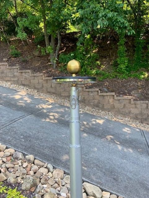 A pole with a gold ball on top of it is sitting on a sidewalk next to a brick wall.