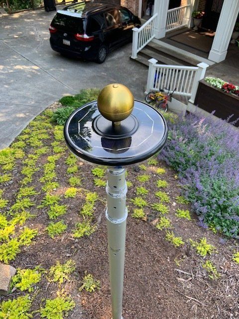 A black car is parked in the driveway next to a pole with a gold ball on top of it.