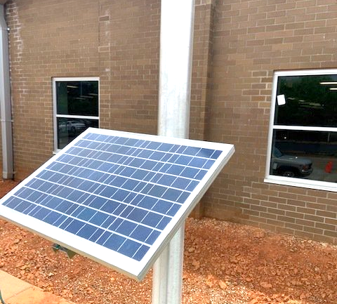 A solar panel on a pole in front of a brick building