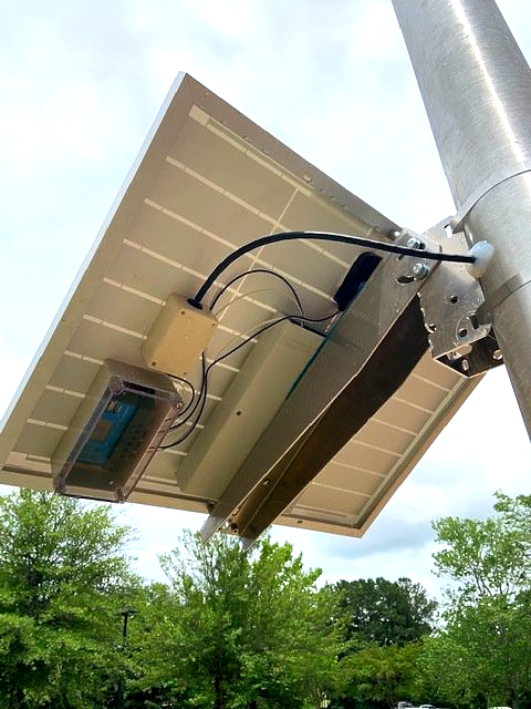 A solar panel is attached to a pole with trees in the background