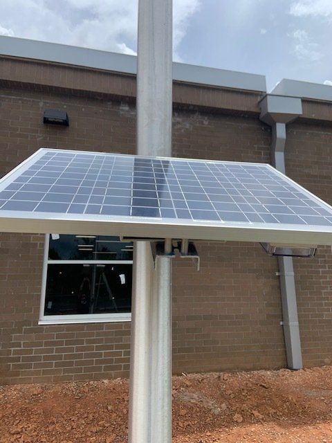 A solar panel is sitting on top of a pole in front of a building.