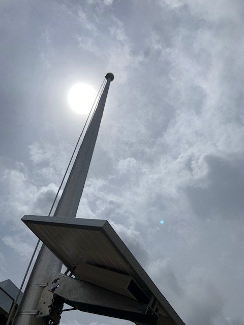 Looking up at a flag pole with the sun shining through the clouds