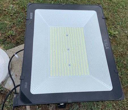A flood light is sitting on top of a concrete post in the grass.