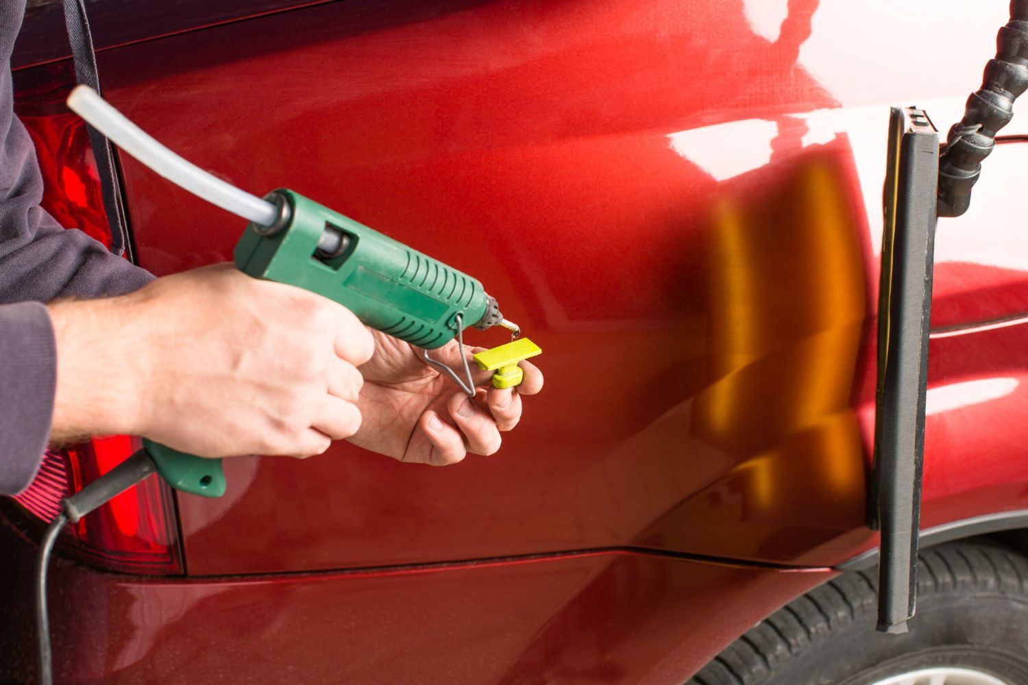 Hands using a green blow dryer to dry a red car door in an auto shop