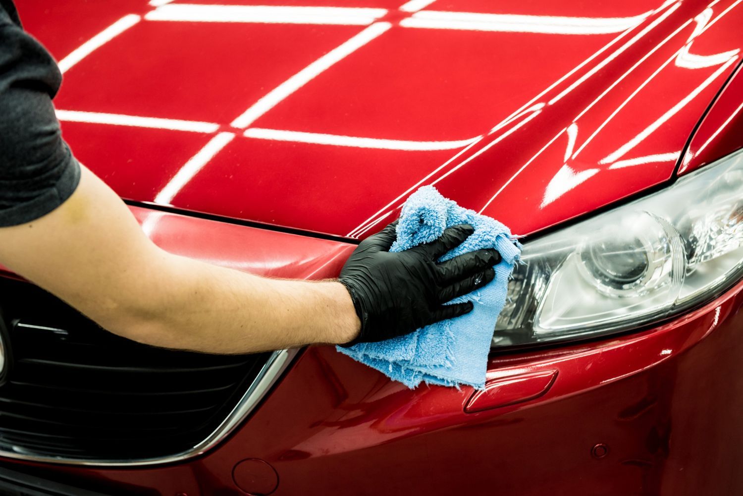 Person wiping a red car’s headlight and fender with a blue cloth