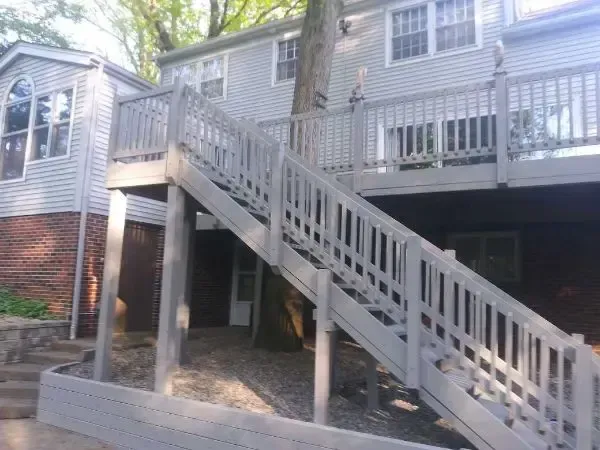 Gray exterior staircase leading to a raised house with white railings and brick siding