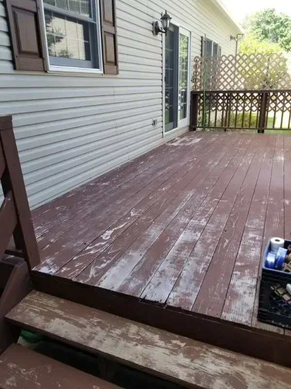 Weathered wooden deck outside a house with a railing, steps, and a lattice fence in the background