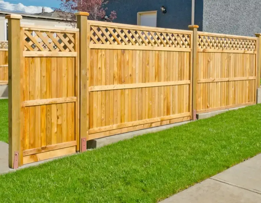 Wooden lattice-top privacy fence along a green lawn beside a sidewalk and house.