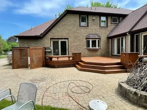 Backyard patio with wooden deck, brick house, lattice fence, and paved courtyard
