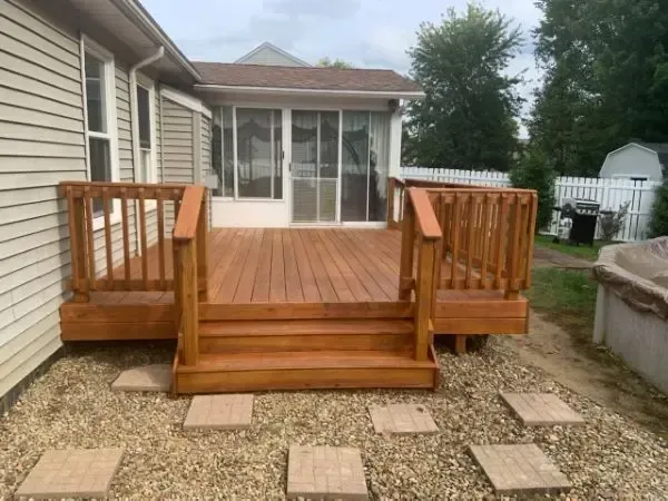 Wooden back deck with steps and railings leading to a screened porch beside a house.