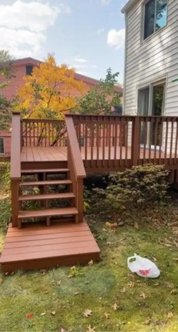 Wooden backyard deck with steps beside a house, autumn trees in the background, and a lawn below.