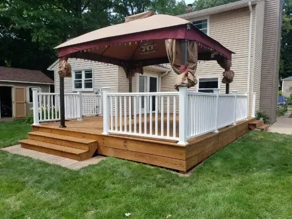 Backyard deck with white railing, steps, and burgundy gazebo beside a house