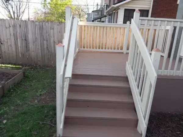 White outdoor staircase with brown steps and railings leading to a raised porch by a house.
