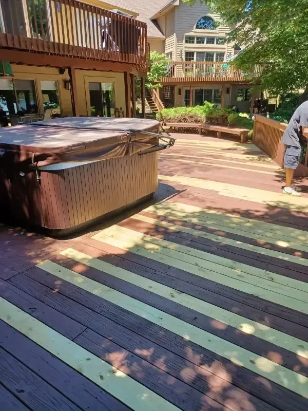 Outdoor deck with a hot tub, wooden railings, and a person standing near the pool area