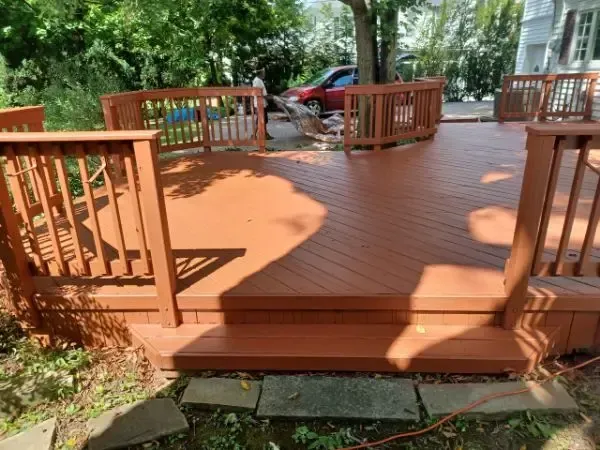 Wooden deck with railings and steps in a leafy backyard, with a red vehicle in the background.